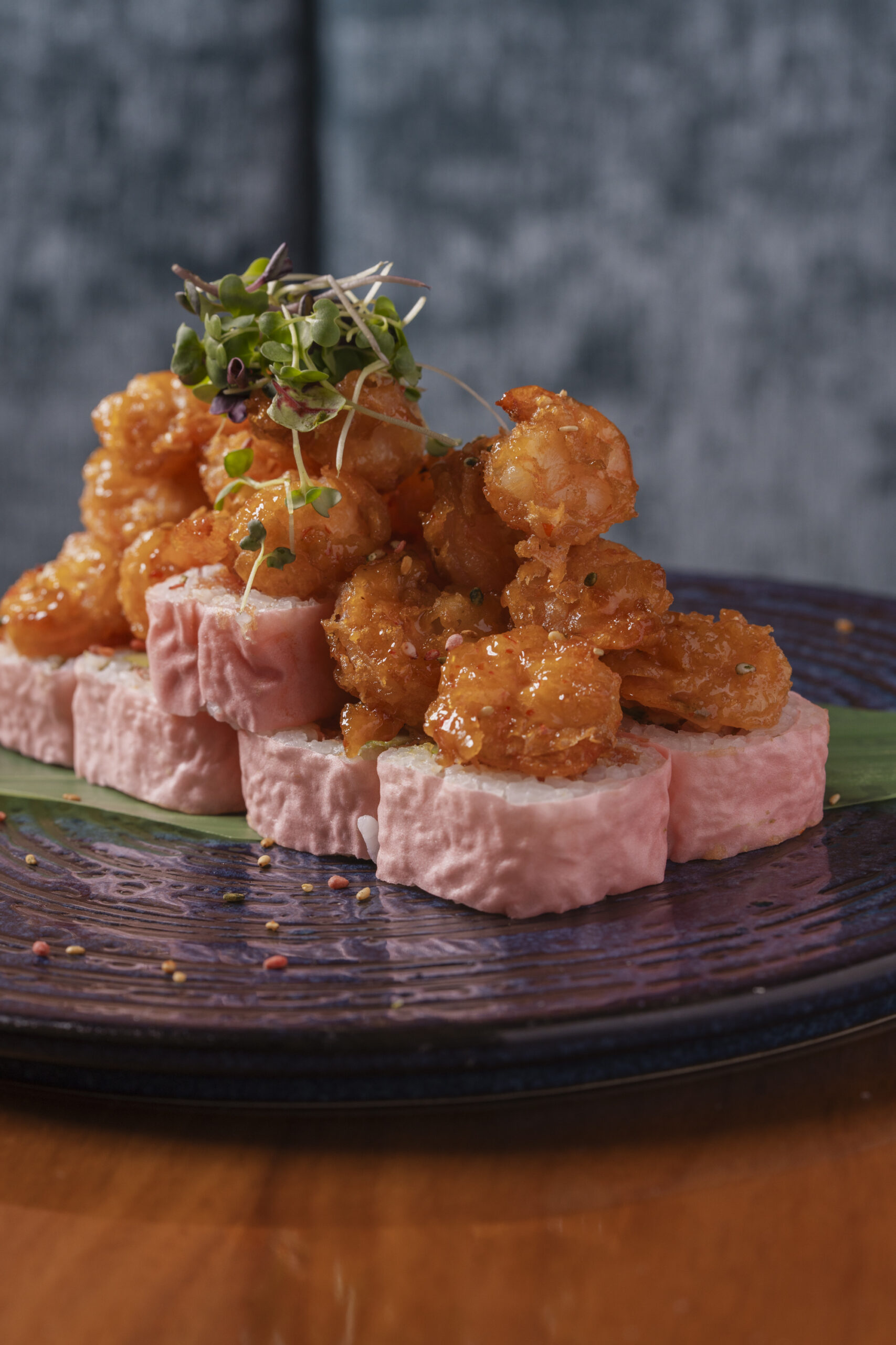 Sushi roll with pink rice wrap topped with crispy glazed popcorn shrimp