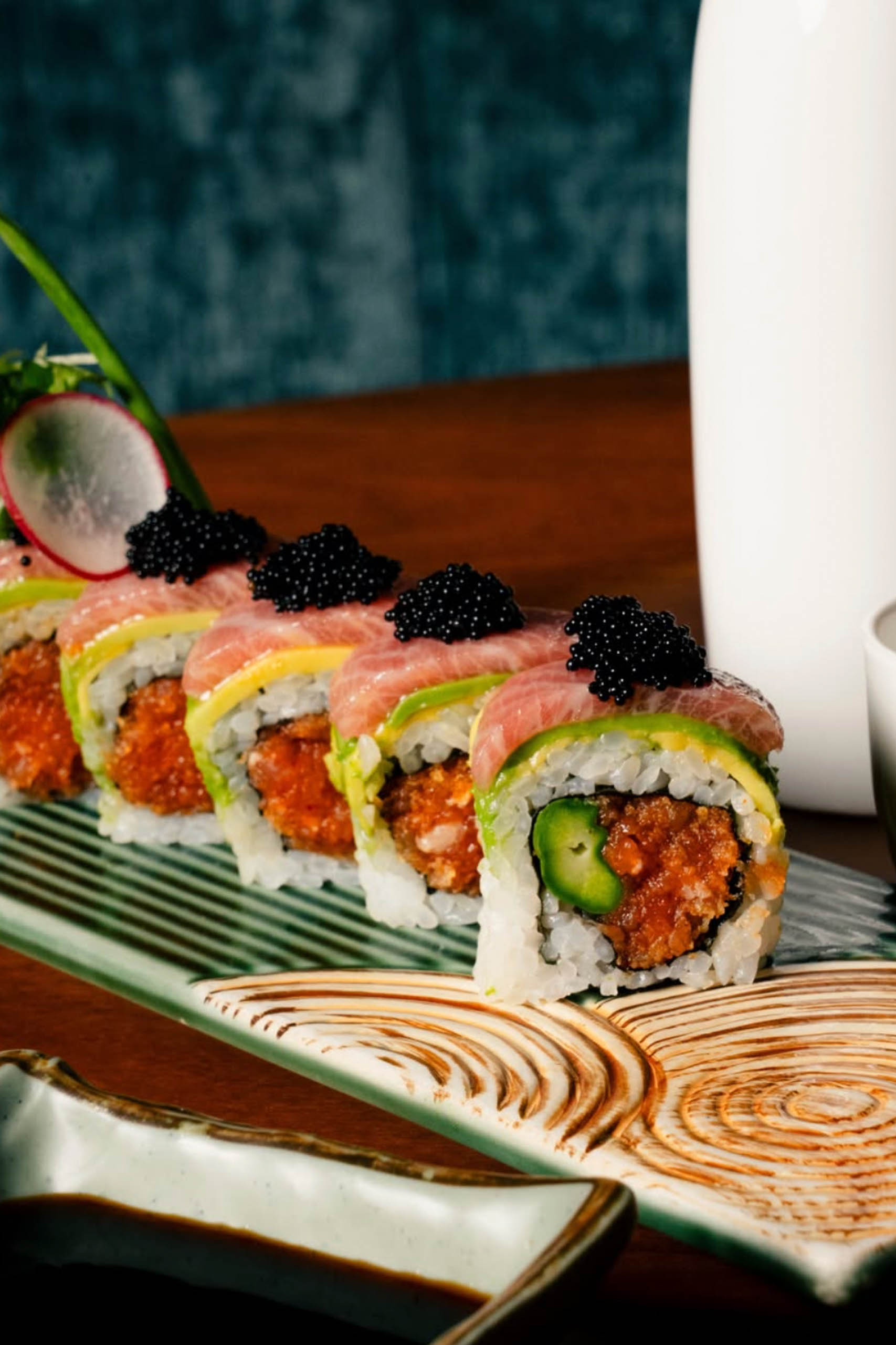 Sliced sushi roll with spicy fish and jalapeño, topped with avocado, fresh tuna, and black caviar